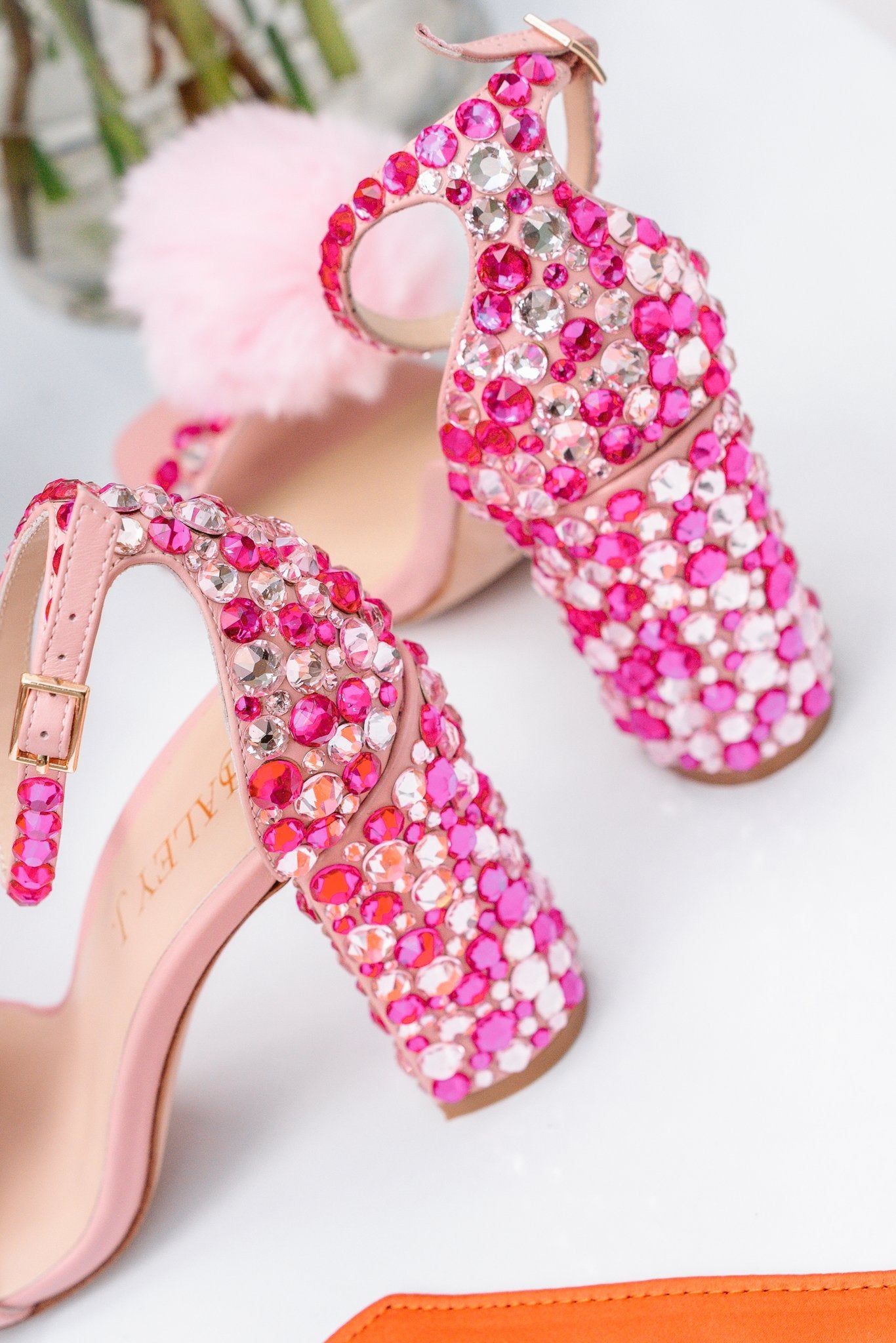 Haley J. Katie Pink Crystal Heel — close-up detail of blush pink block heel sandal completely encrusted in hot pink and clear crystals, with gold buckle ankle strap, Haley J. branded insole, and pink pom pom accent