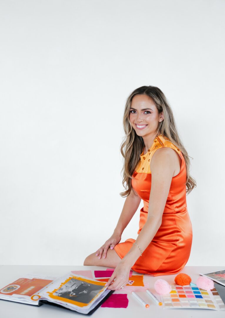 Haley J. in her debut orange dress with a rhinestoned embellished collar planning out her collection with swatches and materials around her.